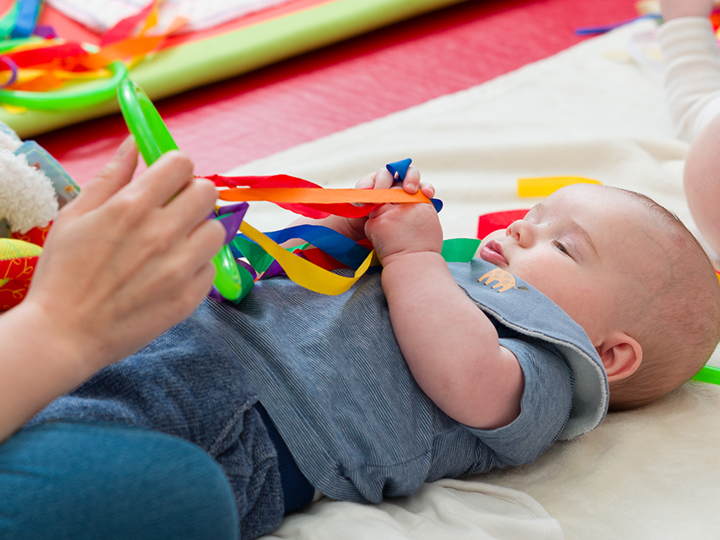 Baby lying on their back on a mat playing with a multi-coloured string toy