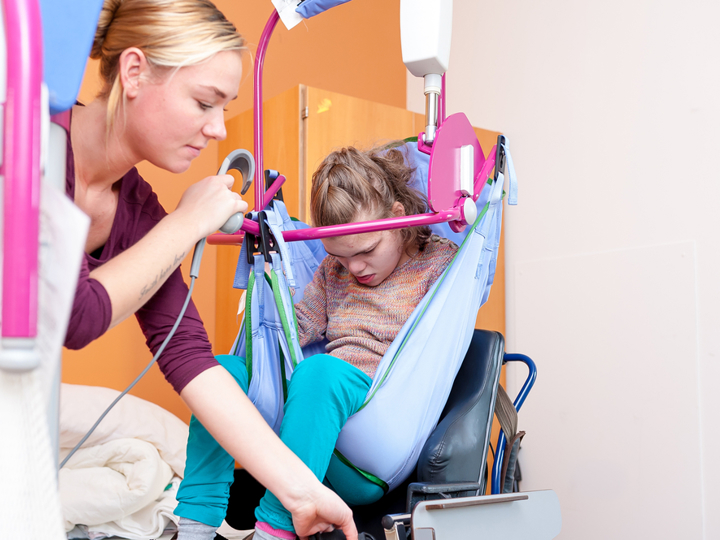 Adult woman helping to adjust a hoist with a child inside the hoist