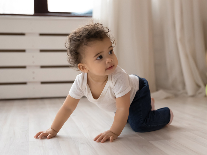 Baby crawling on their hands and knees across the floor.