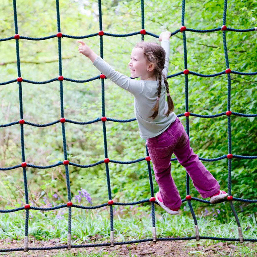 Young girl climbing on a rope net climbing frame in a woodland adventure playground. 