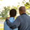 Teenage boy and dad standing with their back to the camera. The dad has his arm around his son.