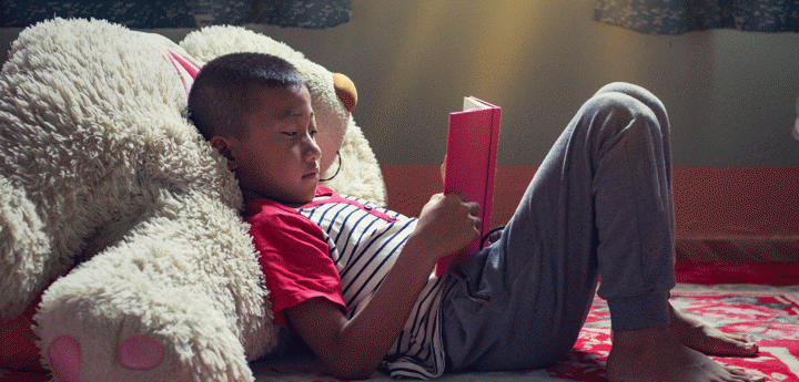 child leaning against teddy bear reading