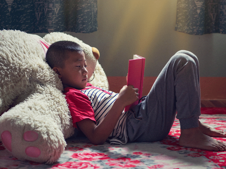 child leaning against a large teddy bear reading
