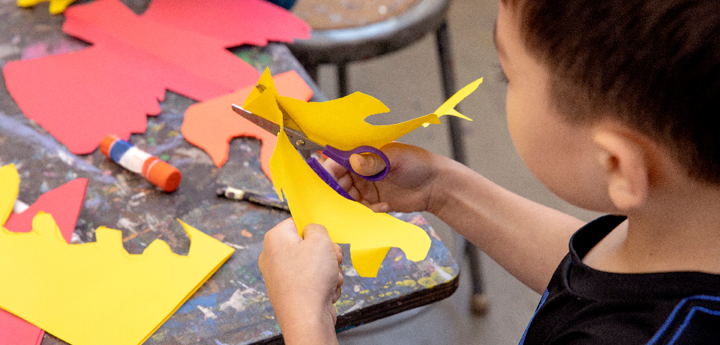 Young boy cutting out yellow paper with scissors