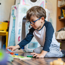Young boy wearing glasses, kneeling on the floor playing with wooden toys.