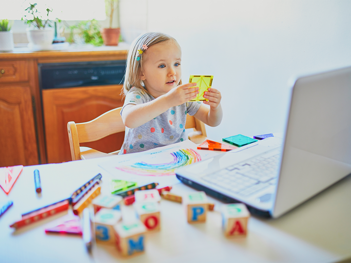Toddler girl sitting on a chair at kitchen table and playing with colourful shapes