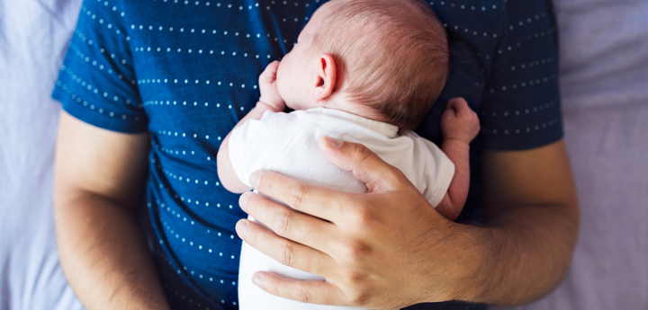 Young baby lying face down on a man's stomach