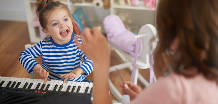 Child playing the keyboard with an adult woman in front of her conducting her