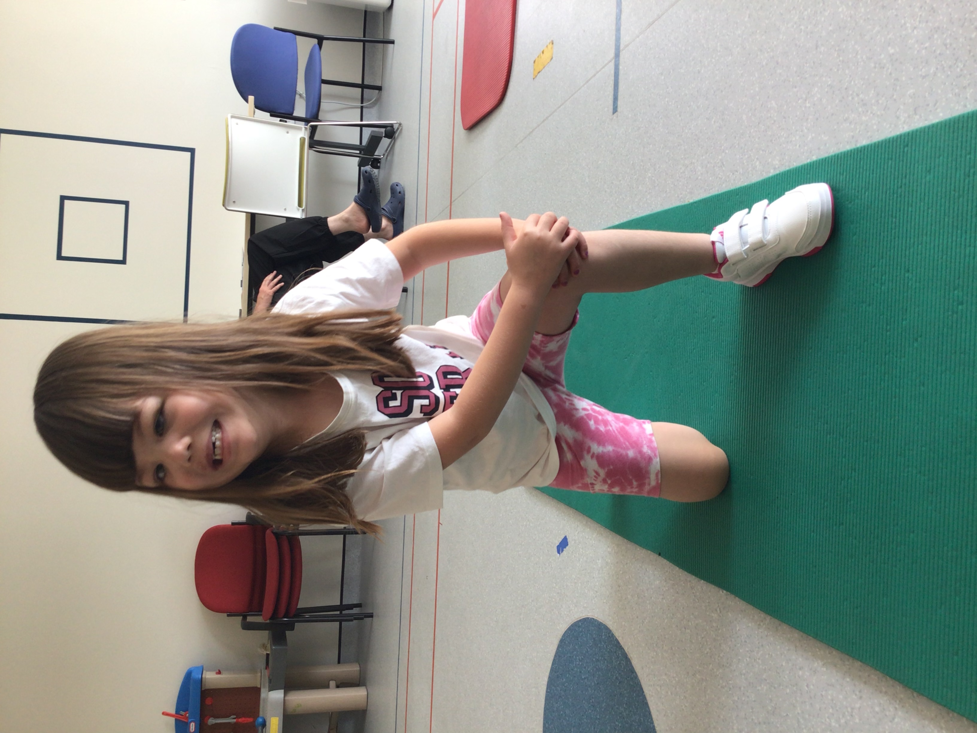 Young girl kneels on a yoga mat with one leg bent forward in front of her and her hands on her raised knee. 