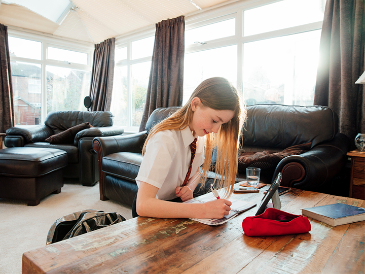 School girl sitting on the floor in living room, leaning on a coffee table doing some homework in a notebook