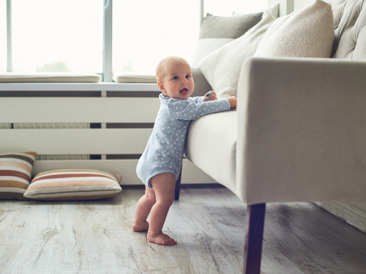 Baby standing up leaning his weight onto a sofa