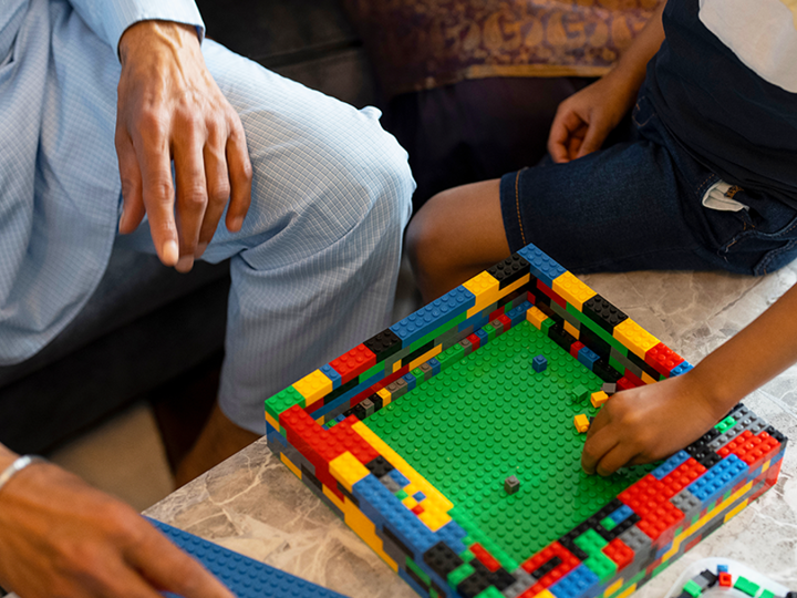 Adult man sitting on sofa and a young boy sitting on the edge of a coffee table, both playing with lego.