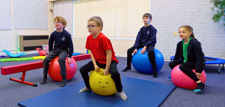 4 Young Children Sitting On Space Hoppers In A Classroom Vibrant