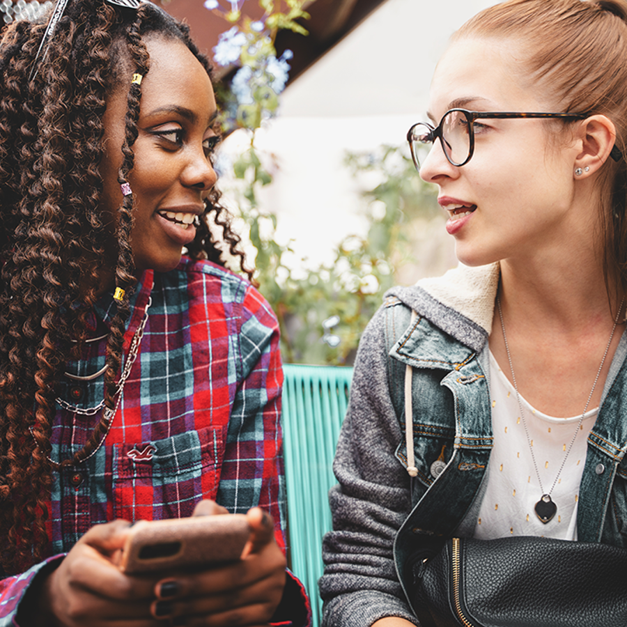 2 teenage girls talking. Girl on left is holding a phone
