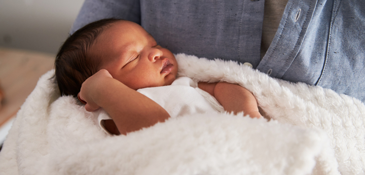 baby asleep in blanket in arms of an adult